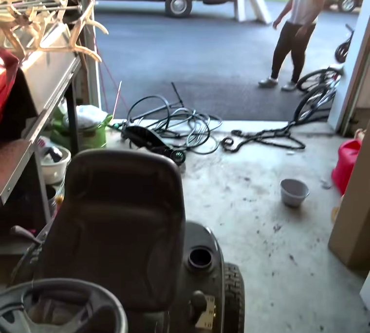 A garage mid-cleanout, a ride-on mower and coiled hose on the floor and the van backed up to the open roller door.